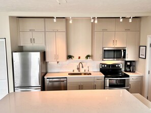 Una cocina moderna con electrodomésticos de acero inoxidable, armarios de colores claros y encimera de mármol.