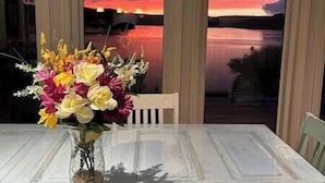 A table with a vase of flowers and a view of a sunset over a body of water.