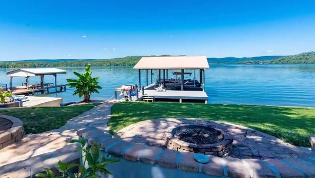 A lakeside property with a dock, outdoor seating, and a fire pit.