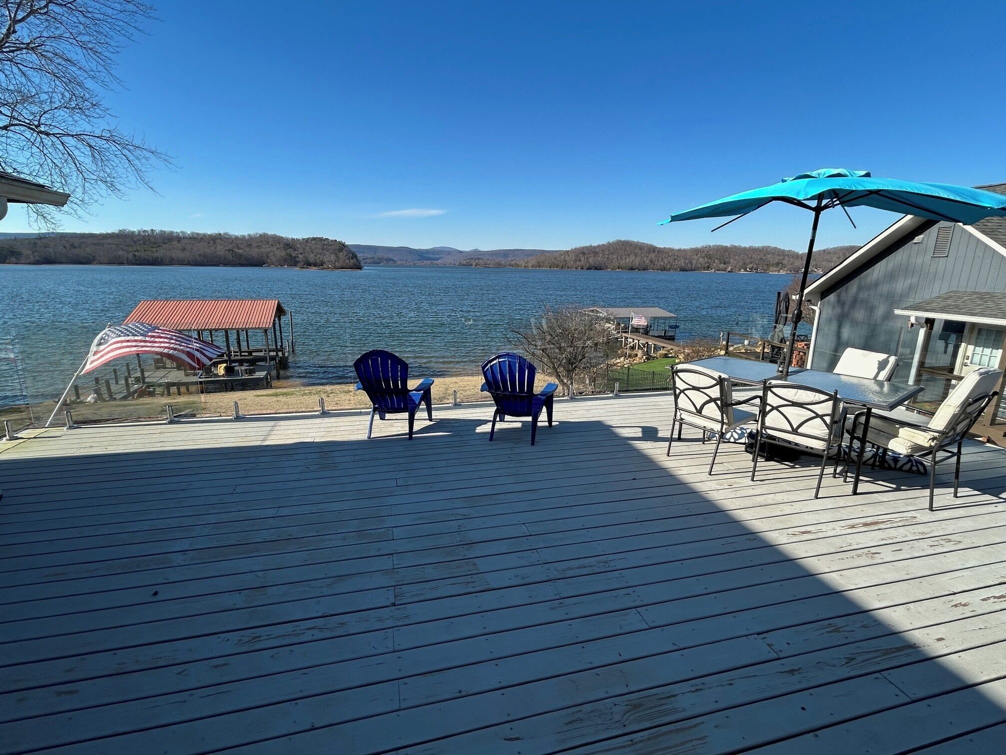 Una terraza de madera con dos sillas Adirondack, una mesa con sillas y un paraguas azul.