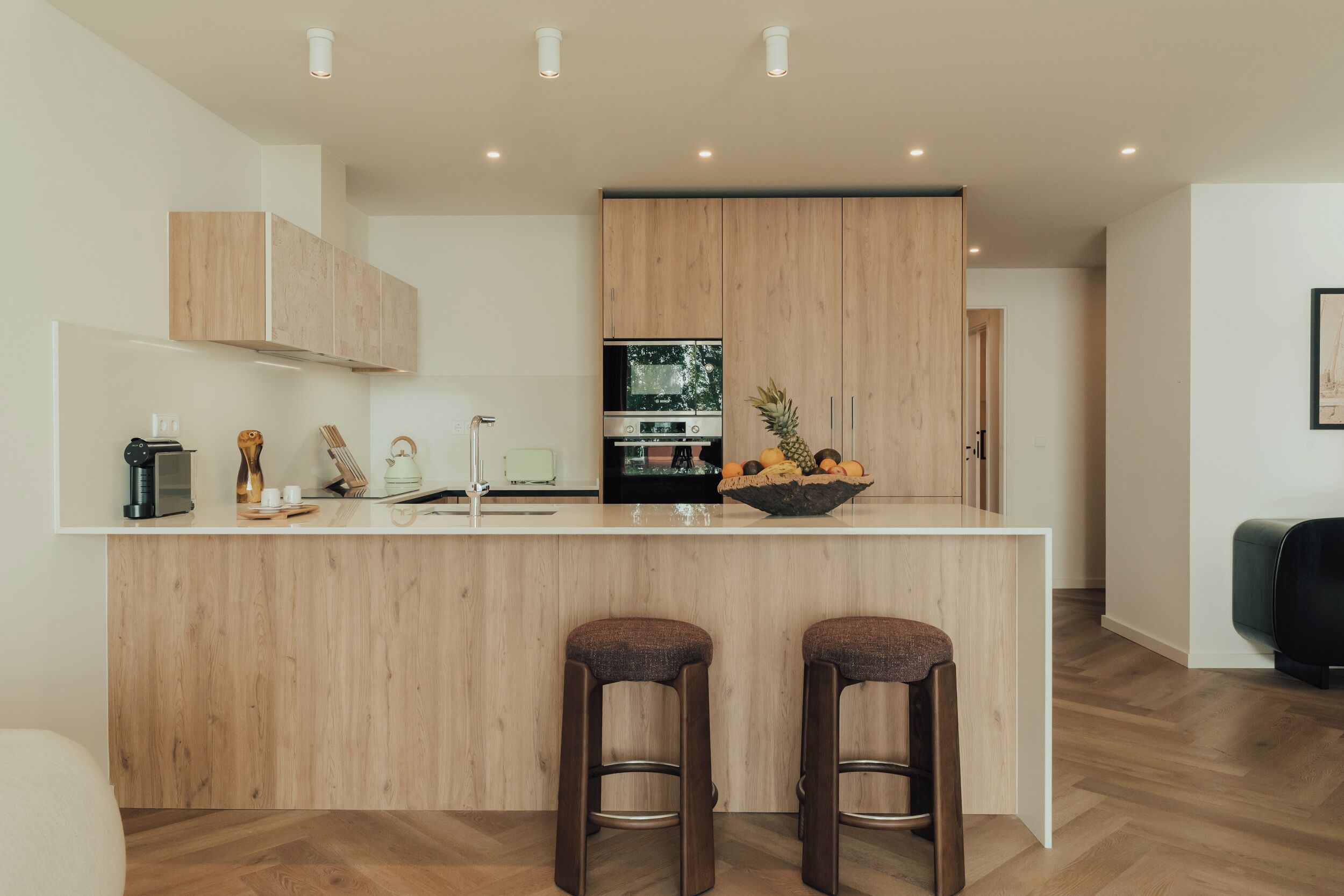 Una cocina moderna con armarios de madera, una isla central con taburetes y un horno empotrado.