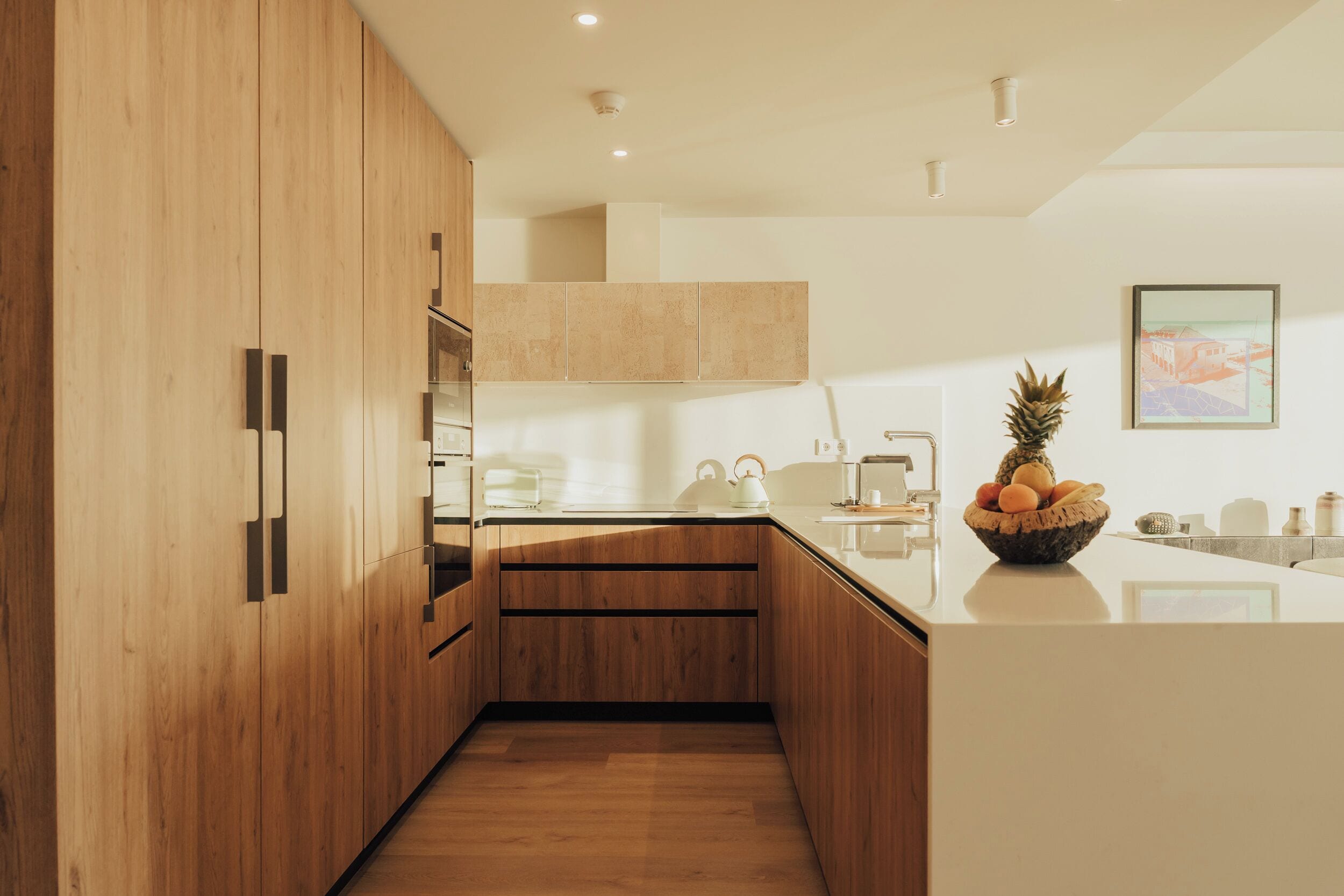 Una cocina moderna con armarios de madera, encimera blanca y frutero.