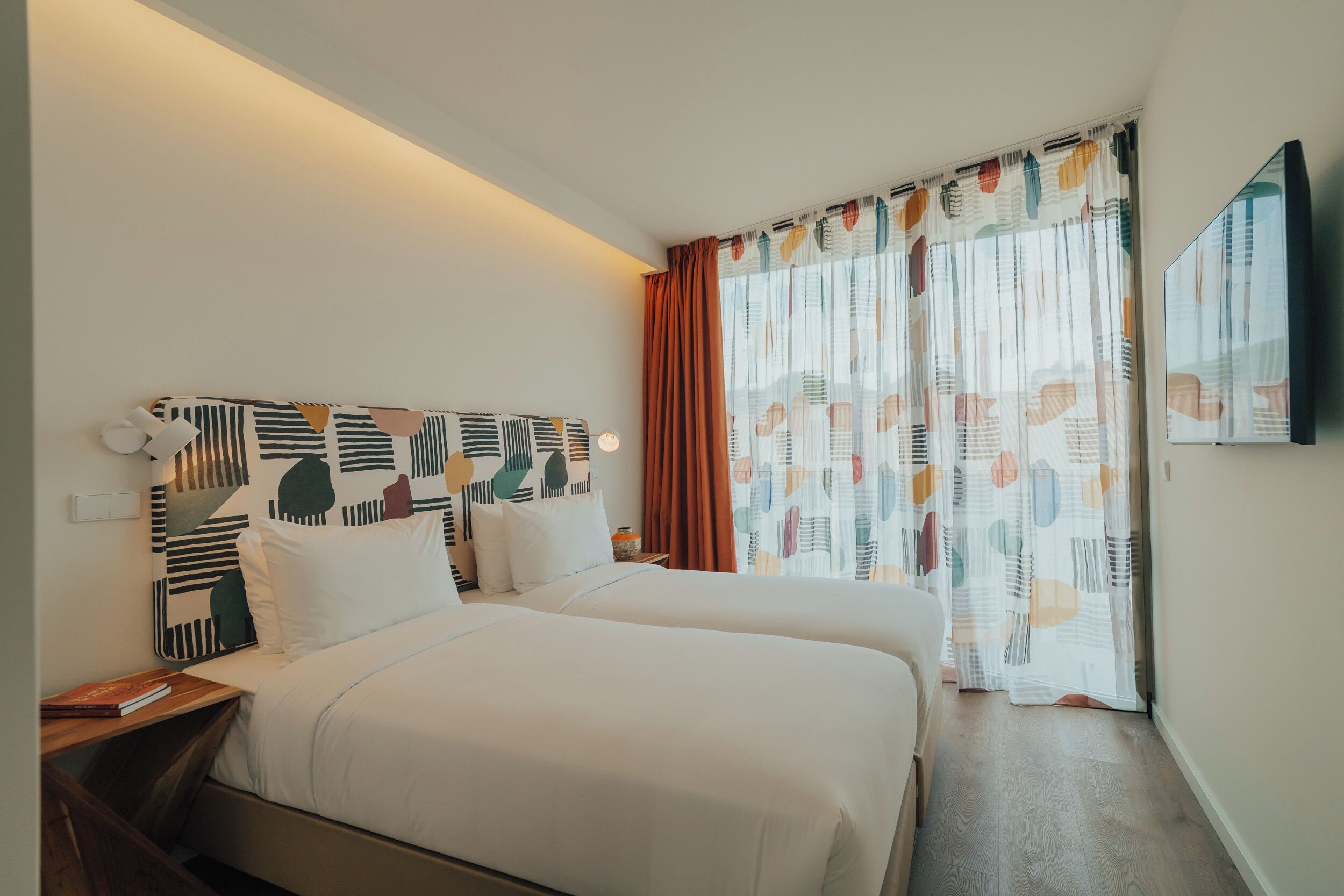 Een hotelkamer met een bed, een nachtkastje, een televisie en een raam met gordijnen.