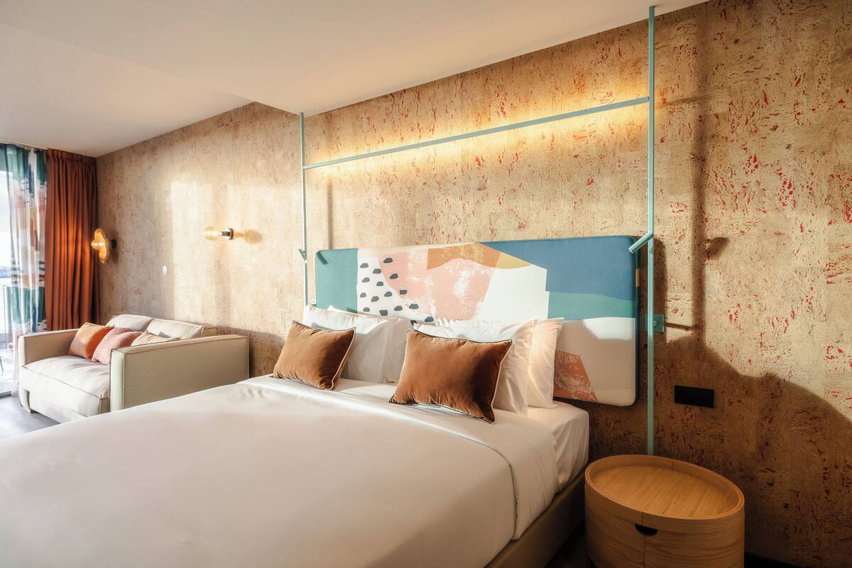 Een moderne hotelkamer met een groot bed, een bank, een houten bijzettafeltje en een kunstwerk aan de muur.