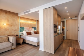 Quarto de hotel moderno com cama, sofá, cozinha compacta e banheiro.