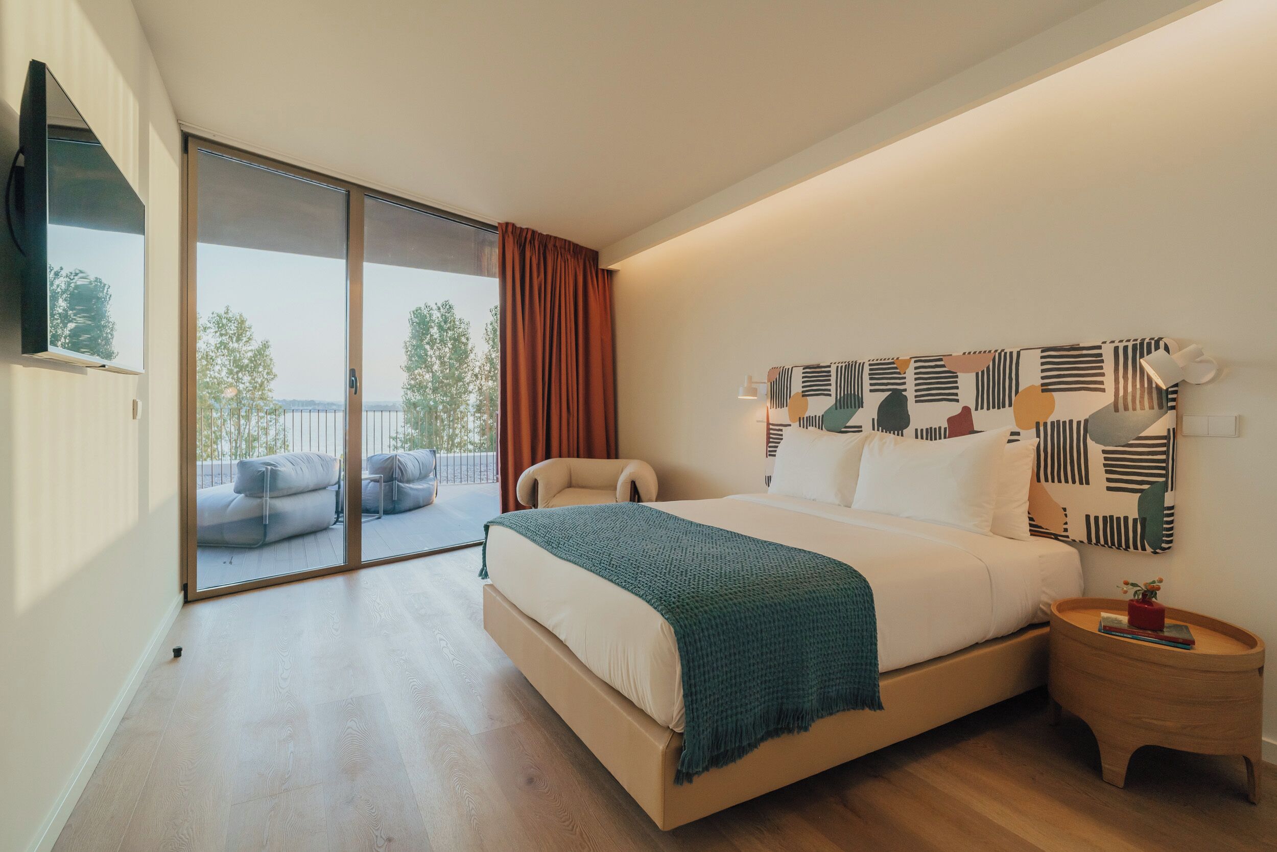 Un dormitorio moderno con una cama grande, vistas al exterior y una mesita de noche pequeña.