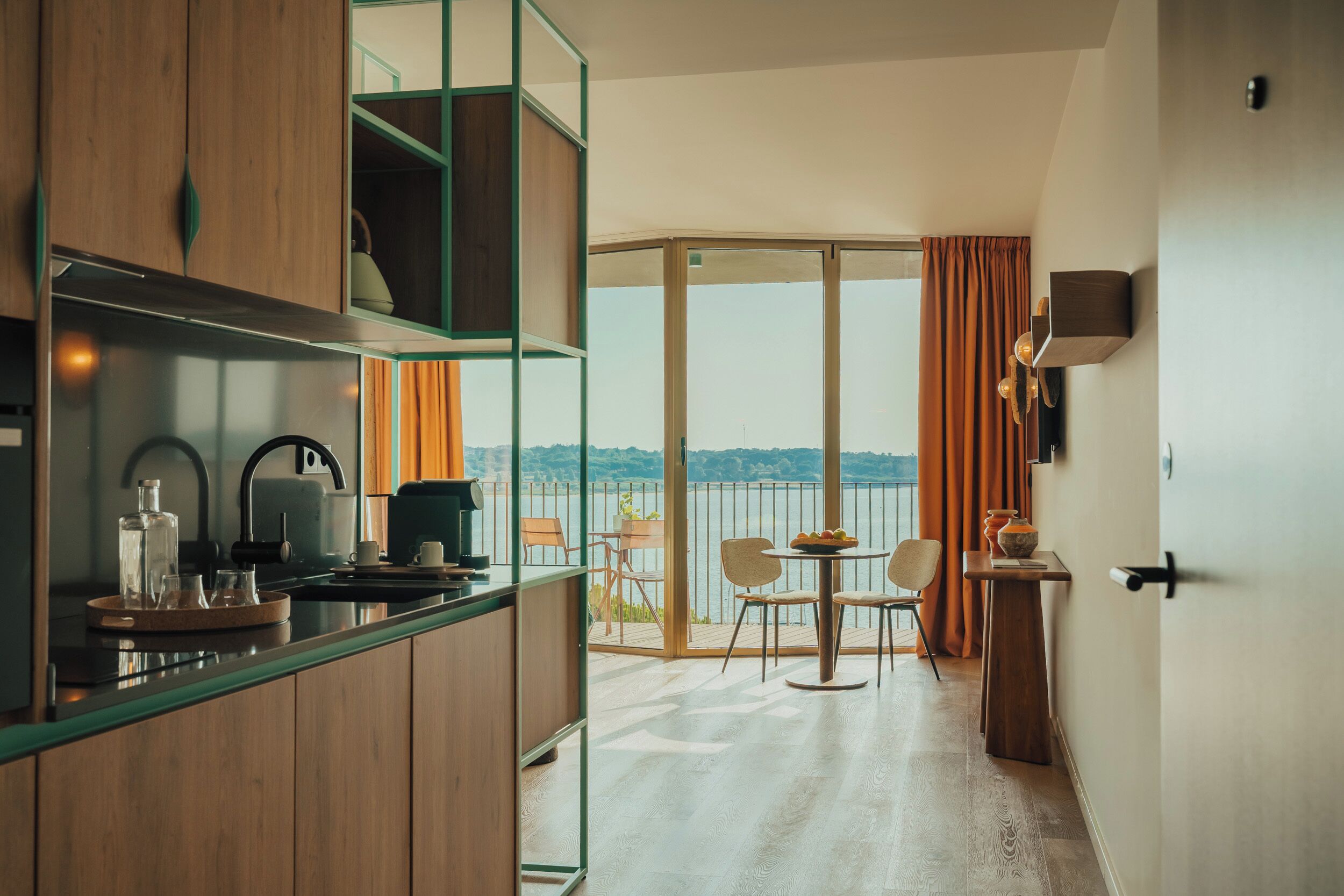 Una cocina moderna con vistas a un balcón, un comedor con sillas y una mesa con frutero.