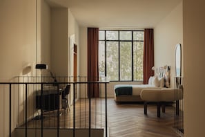 A hotel room with a bed, a desk with a chair, a window with curtains, and a railing.