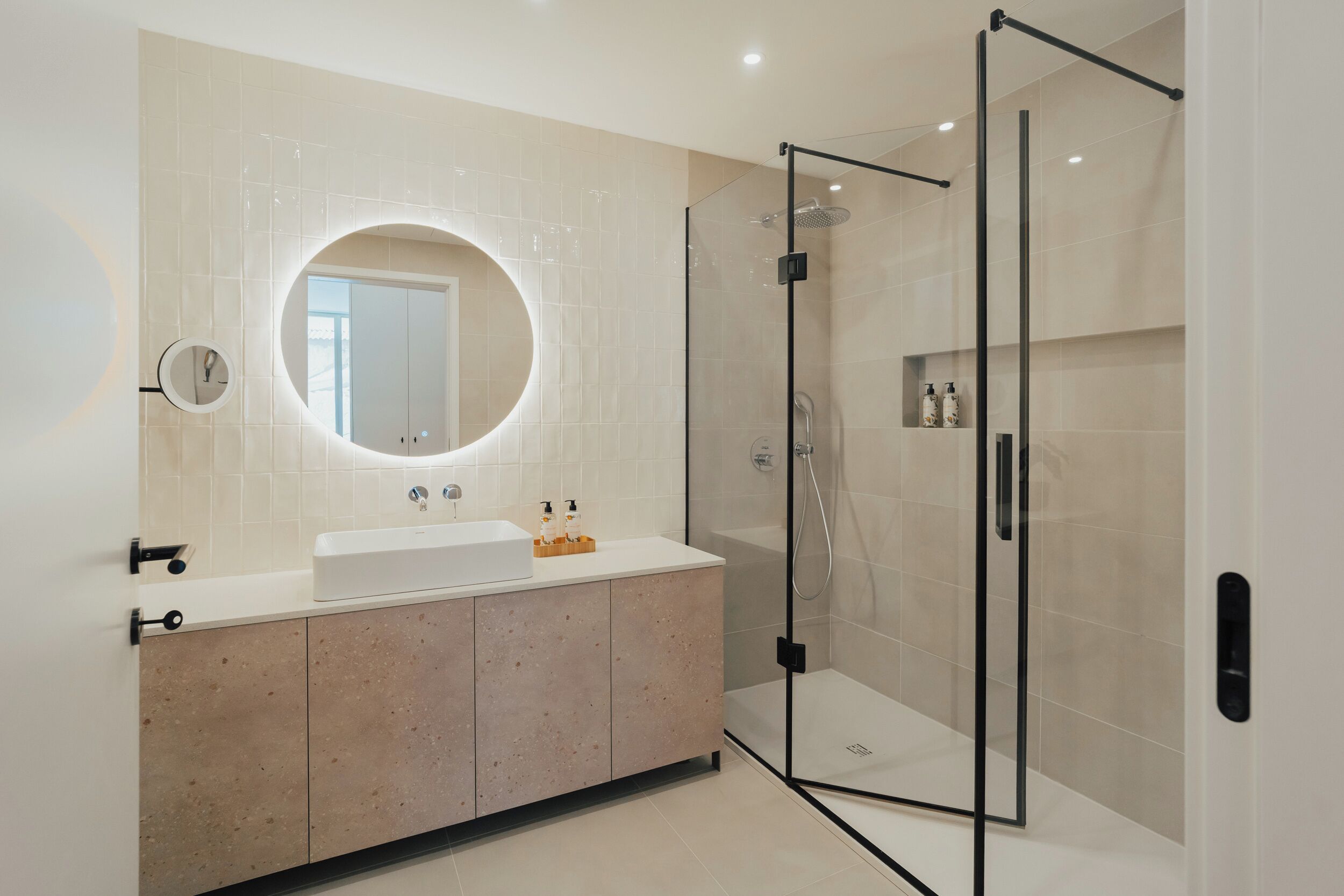 A modern bathroom with a glass-enclosed shower, a round mirror, and a vanity with a sink.