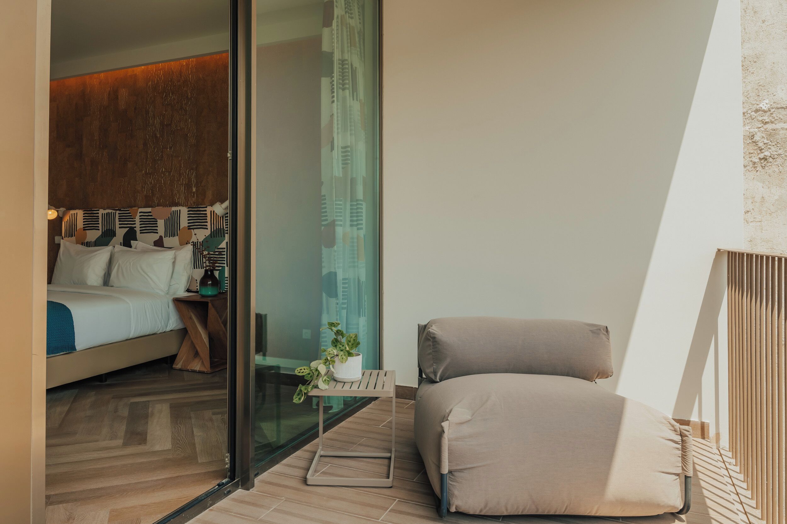 A modern bedroom with a bed, a bedside table, a potted plant, and a view through a glass door.