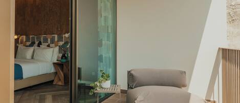 A modern bedroom with a bed, a bedside table, a potted plant, and a view through a glass door.
