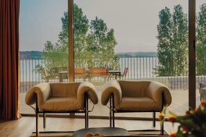 Een kamer met uitzicht op een wateroppervlak, twee fauteuils, een klein tafeltje en een blik op bomen.