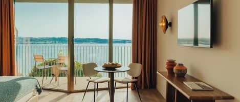 Une chambre d’hôtel avec un balcon, une table à manger, des chaises, un lit, une télévision et des objets de décoration.