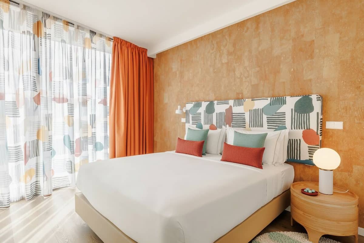 Een moderne slaapkamer met een groot bed, oranje gordijnen en een kamerhord met een patroon.