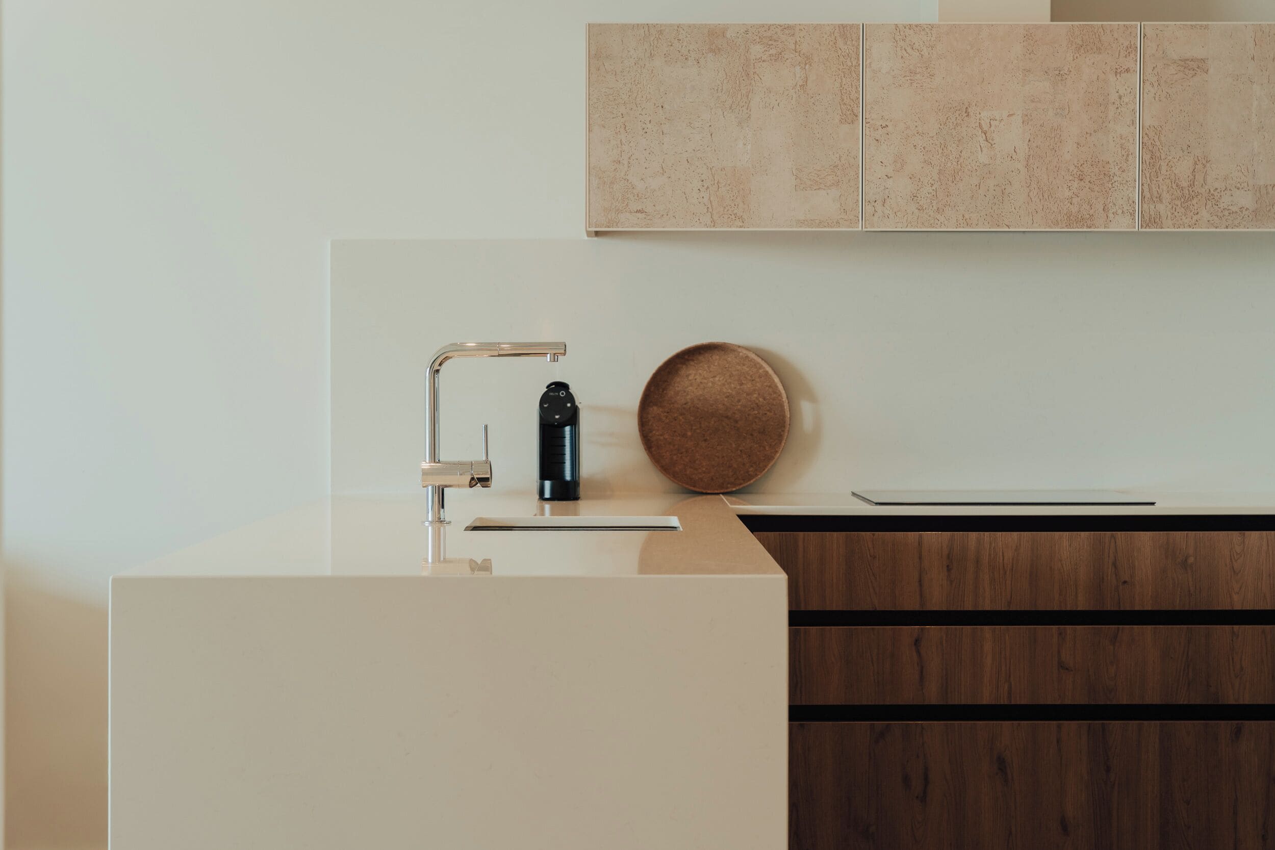 Una cocina moderna con encimera blanca, grifo de acero inoxidable, dispensador de agua negro y un posavasos redondo de corcho.