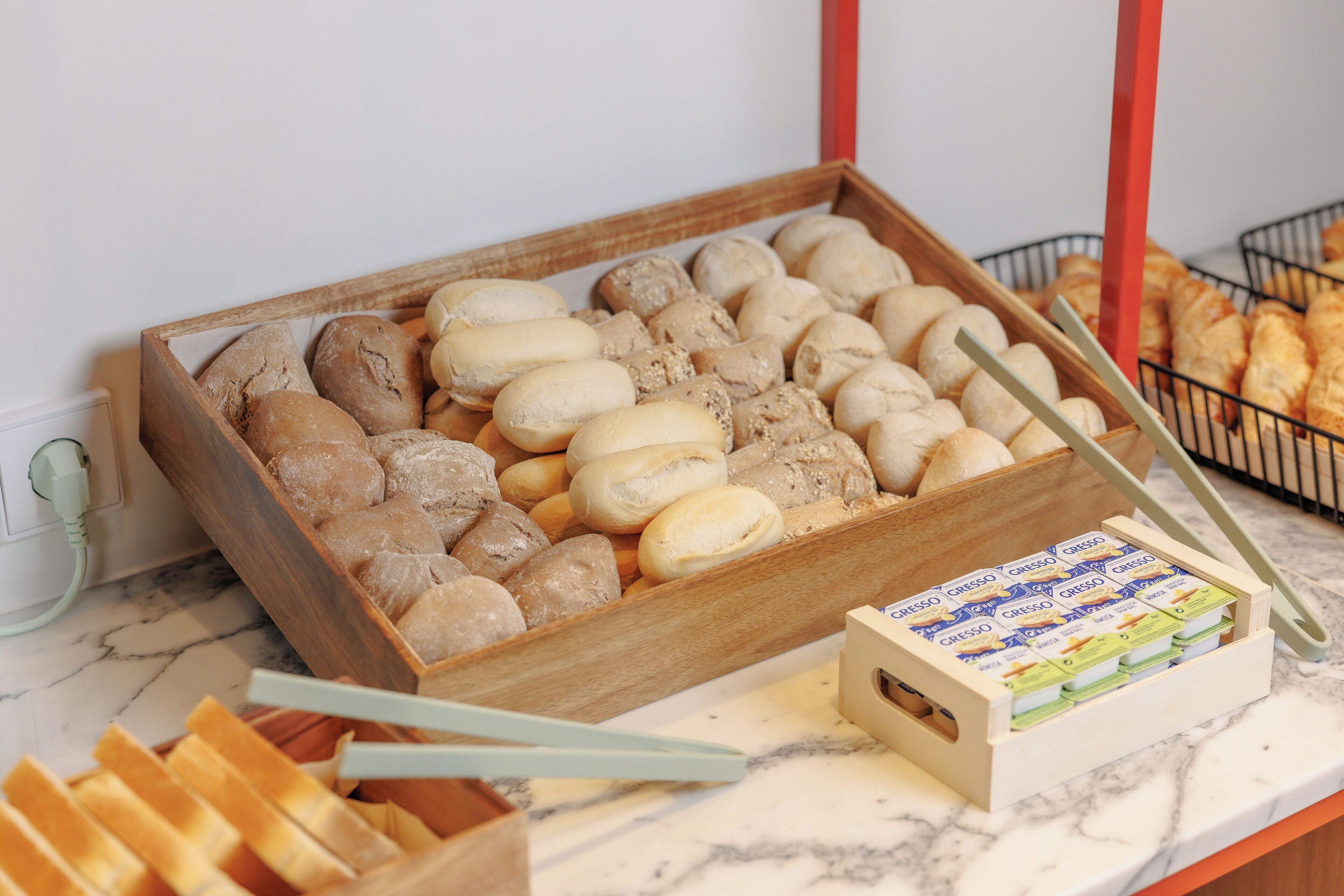 A wooden tray of assorted breads and a box of Caffè Lungo coffee on a marble countertop.
