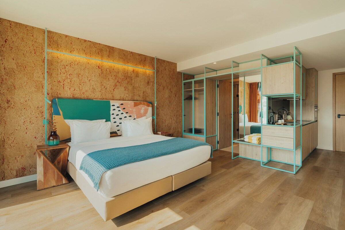 Un dormitorio moderno con una cama grande, un armario con puertas de vidrio y una kitchenette visible.