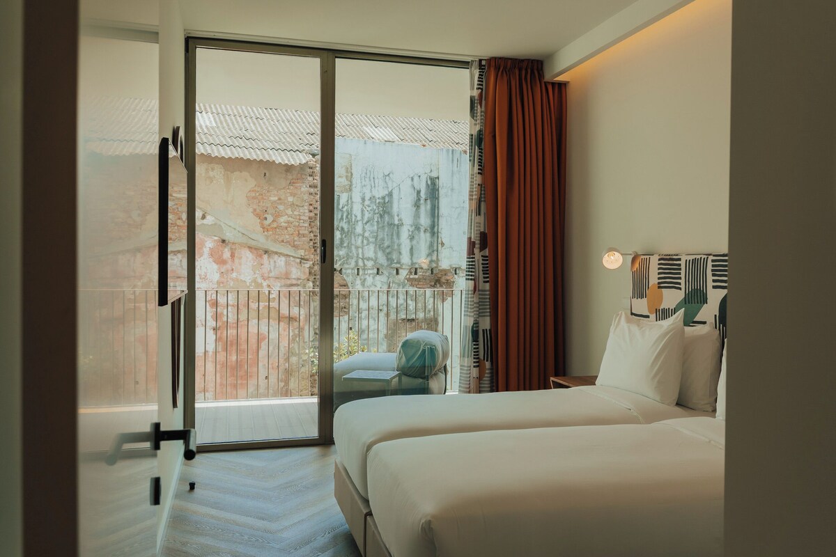 Habitación de hotel con una cama, un pequeño rincón de descanso y vistas a un espacio exterior con barandilla.