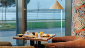 Een ontbijttafel met uitzicht op een waterpartij, een lamp en een kleurrijke muur.