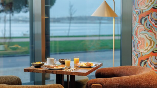A breakfast table with a view of a body of water, a lamp, and a colorful wall. - Upon Harbor - Seixal Bay Hotel (Seixal)