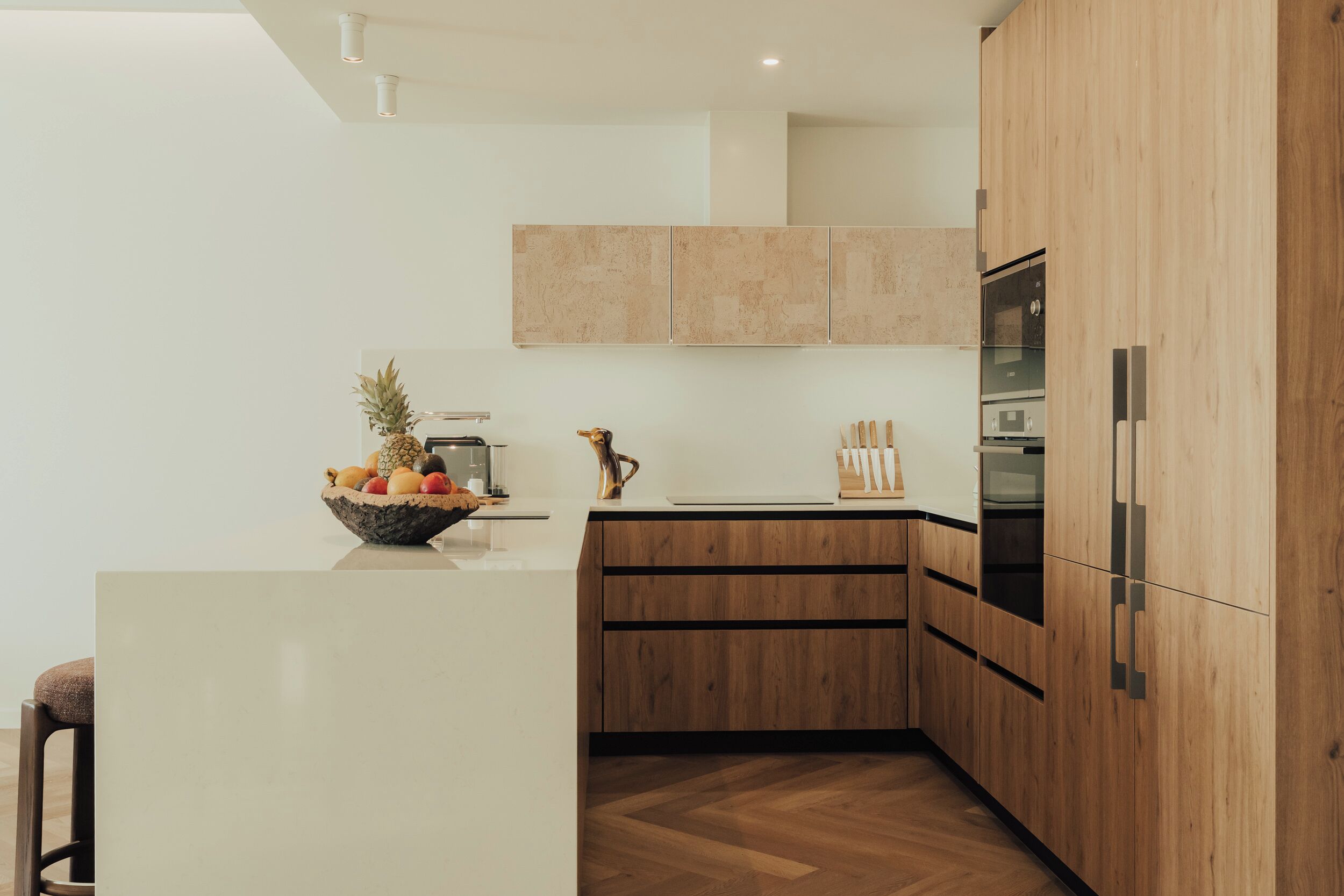 Eine moderne Küche mit Holzausstattung, einer zentralen Kochinsel mit Obstschale und integrierten Geräten.