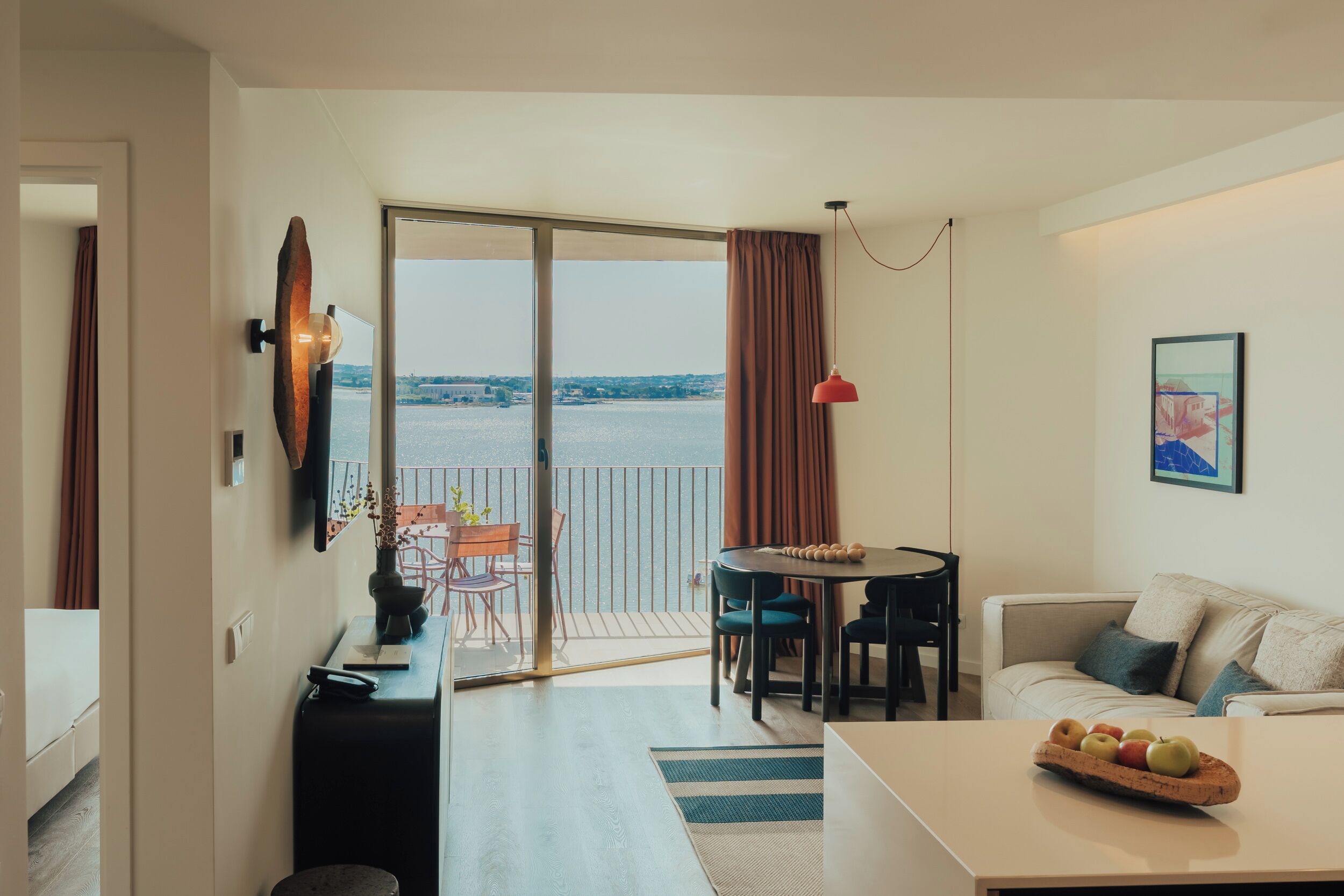Un soggiorno moderno con divano, tavolo da pranzo con sedie, angolo cottura e balcone con vista sull'acqua.
