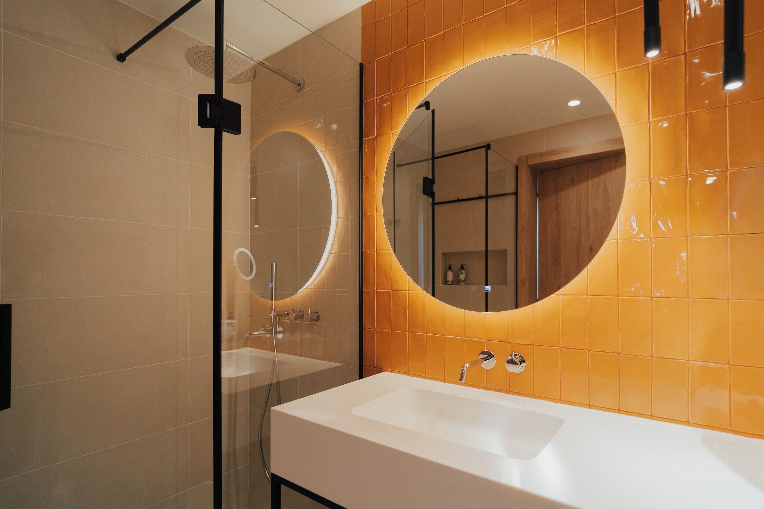 A modern bathroom with a large oval mirror, a white sink, and a glass shower enclosure.