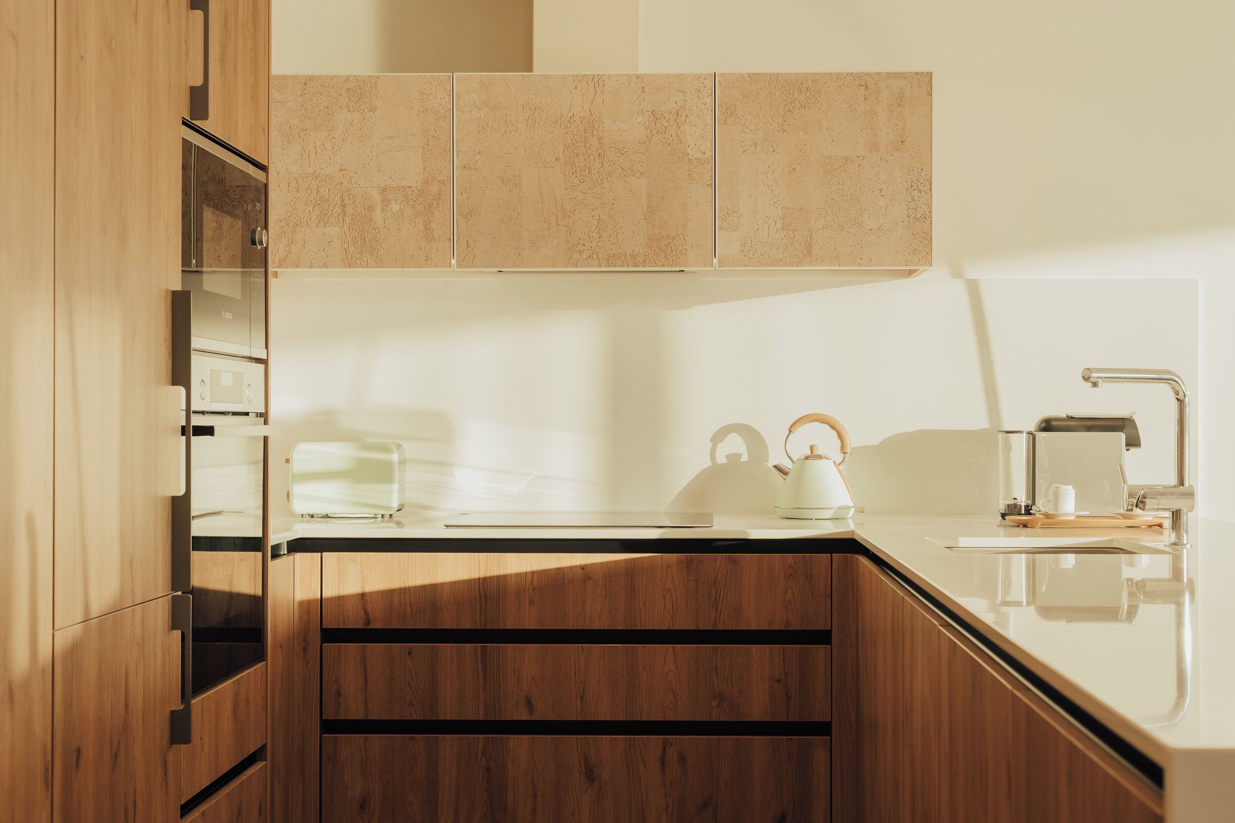 A modern kitchen with wooden cabinets, a countertop, a kettle, and a coffee machine.