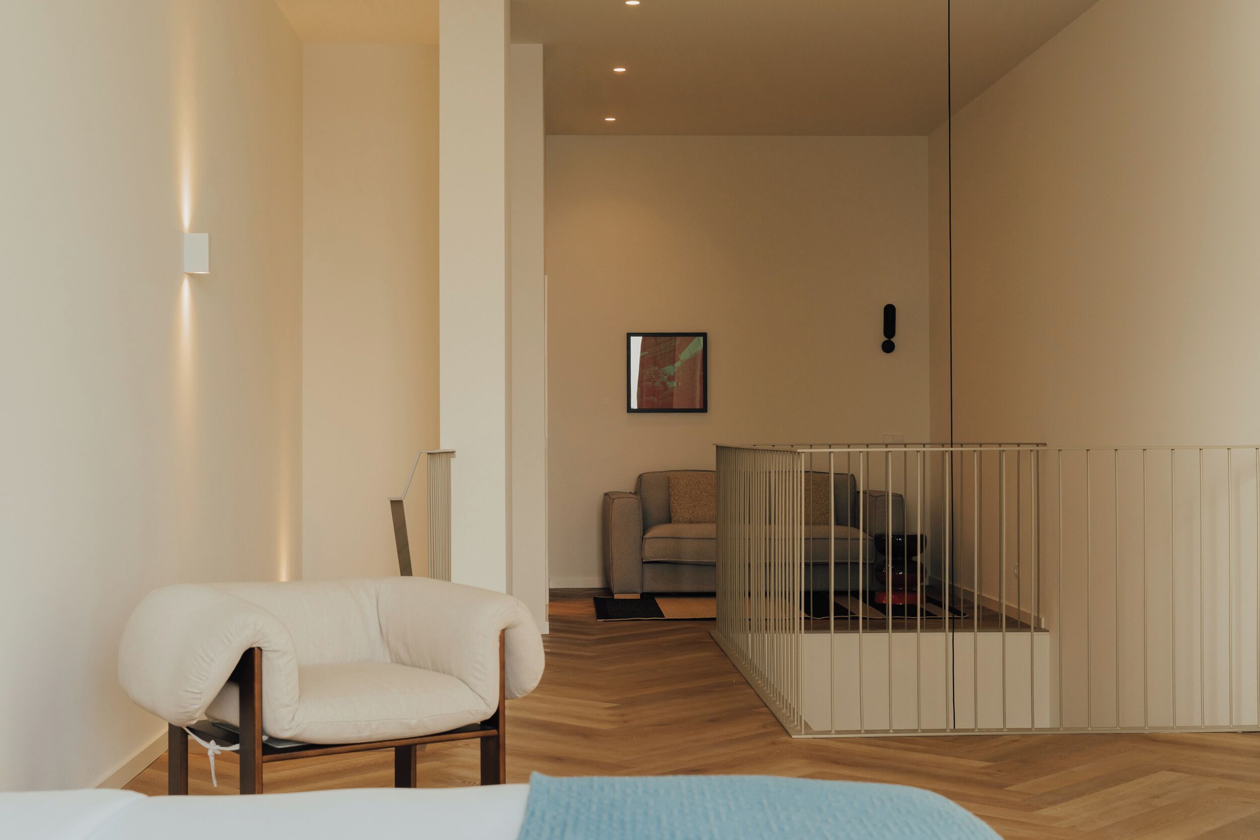 A modern room with a wooden floor, a white chair, a bed, and a small enclosed area with a metal railing.