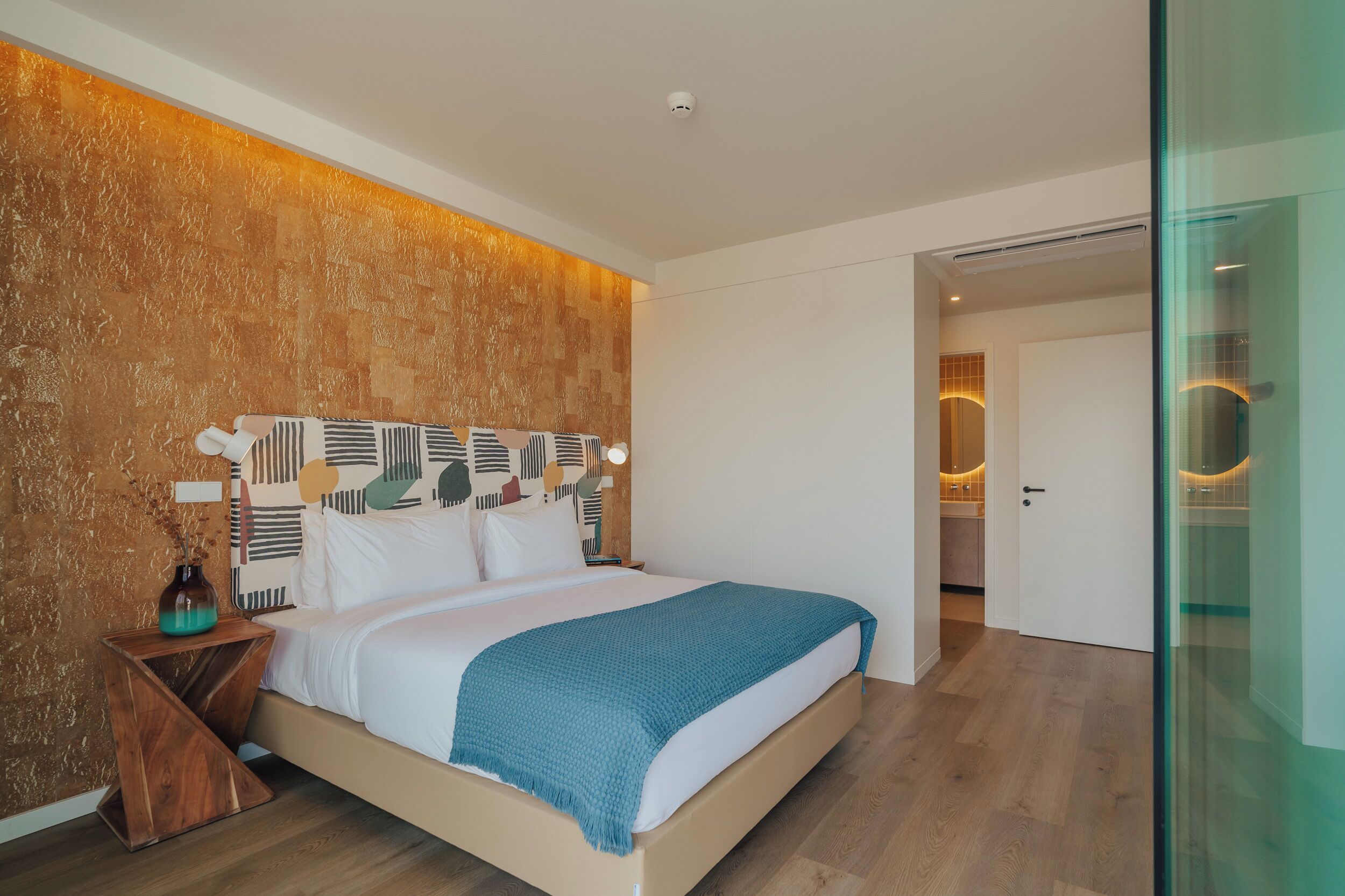 Un dormitorio moderno con una cama grande, una mesita de noche, un florero y una pared con textura.