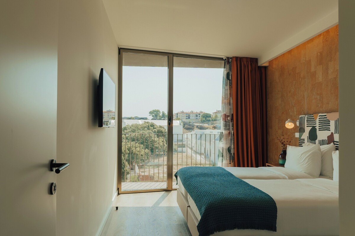 Habitación de hotel moderna con balcón, cama, televisor y vistas a la ciudad.
