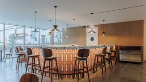 A modern bar area with a curved counter, multiple bar stools, and pendant lighting. - Upon Harbor - Seixal Bay Hotel (Seixal)