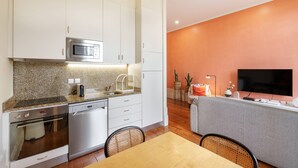 Una cocina moderna con armarios blancos, microondas, horno y lavavajillas. Hay un comedor con mesa y sillas.