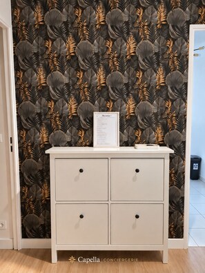 A white cabinet with four drawers against a wall with a leaf pattern wallpaper.