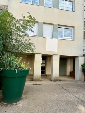 A building with a flat facade, multiple windows, and a ground-level entrance. There is a large green plant in the foreground.