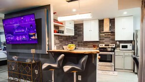 Una cocina moderna con barra, televisor de pantalla plana y comedor con candelabro.