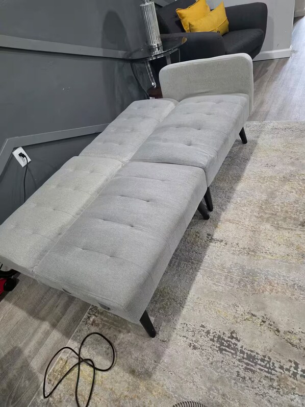 Un sofá gris con diseño capitonado, sobre una alfombra estampada.