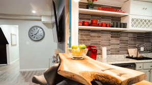 Una cocina moderna con una isla de madera, un reloj en la pared y un letrero que dice 'KISS THE COOK' sobre los estantes.
