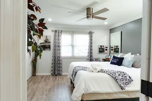 Une chambre à coucher moderne, avec un lit, un ventilateur de plafond et une fenêtre avec des rideaux.