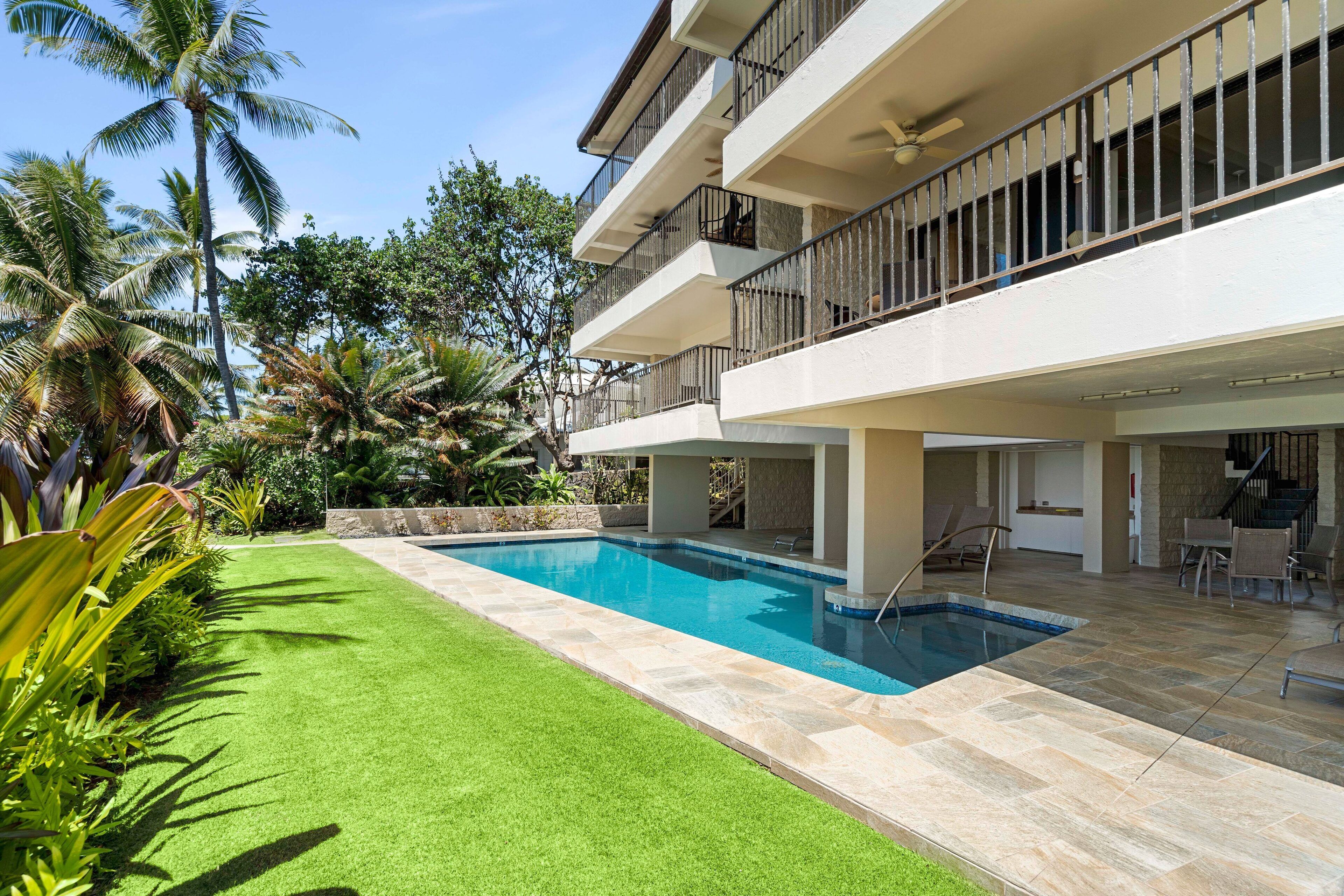 A modern building with a swimming pool, outdoor seating, and lush greenery.
