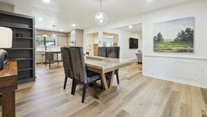 Un comedor moderno con una mesa y sillas de madera, una lámpara colgante y un cuadro de paisaje en la pared.