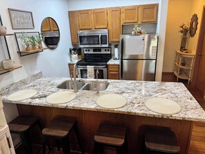 A kitchen with wooden cabinets, a stainless steel refrigerator, a microwave, and a stove. There are three stools at the island. - Penthouse at Notch (First Responder Owner) (Branson West)
