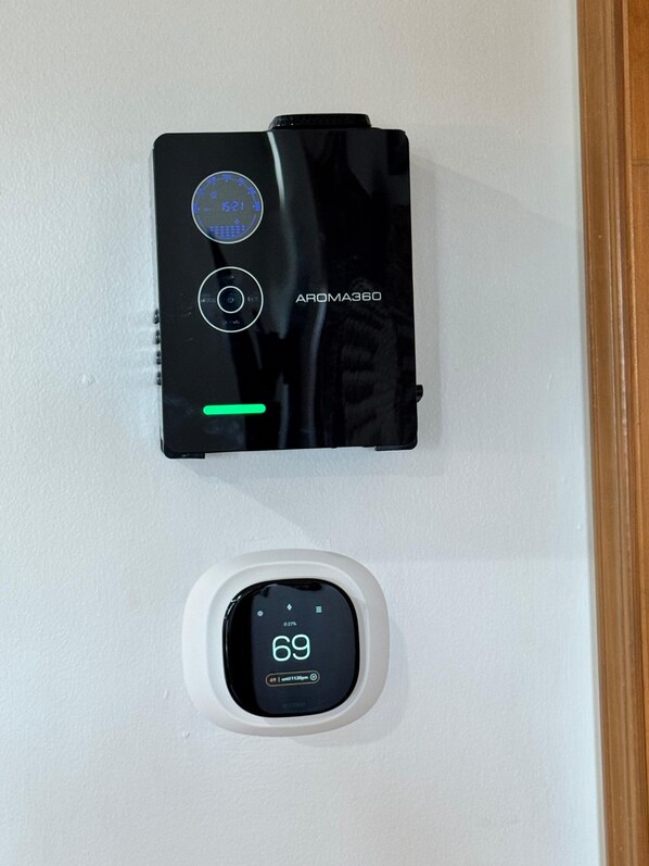 Un purificateur d’air noir et un thermostat numérique fixés sur un mur blanc.