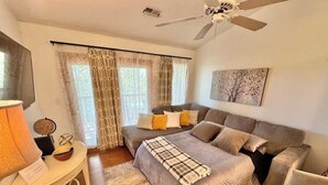 Une chambre à coucher avec un lit, deux canapés, un ventilateur de plafond et une grande fenêtre avec des rideaux.