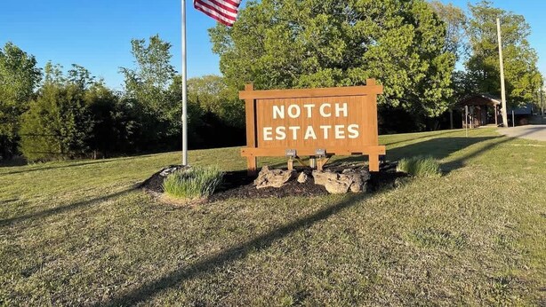 Un panneau en bois sur lequel on peut lire « NOTCH ESTATES », un drapeau américain et, au fond, un kiosque.