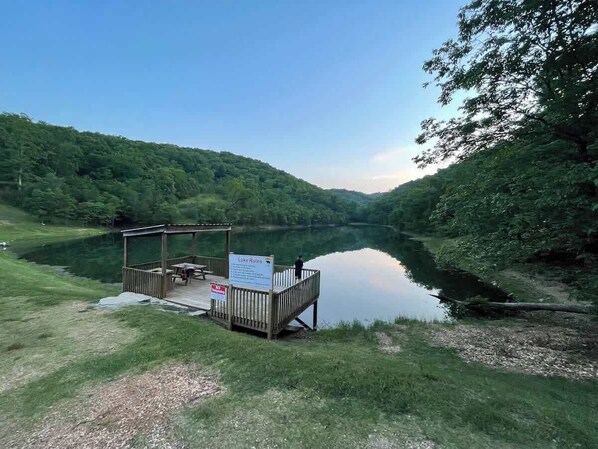 A lakeside wooden dock with a covered seating area and a sign indicating lake rules.