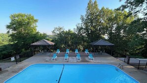 Une piscine rectangulaire avec un plongeoir au centre, entourée de chaises longues et de deux espaces abrités.