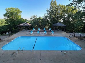 A rectangular swimming pool with a diving board in the center, surrounded by lounge chairs and two covered areas.
