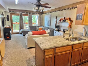 Un salon chaleureux avec une cheminée, un coin repas et une cuisine dotée de meubles en bois et d’un plan de travail en marbre.