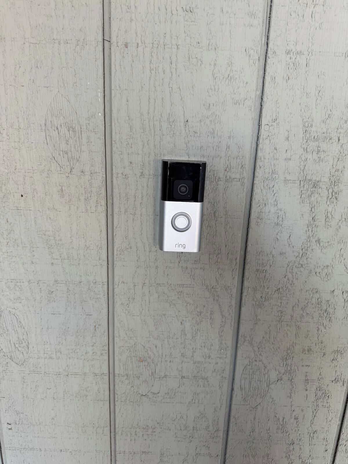 Une sonnette dotée d’une caméra et d’un bouton d’appel, le tout installé sur une porte à surface texturée.